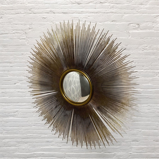 Decorative wall mirror with sunburst design on a textured white wall