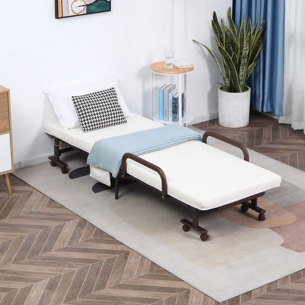 Foldable bed in a room with a plant and books on a small table.
