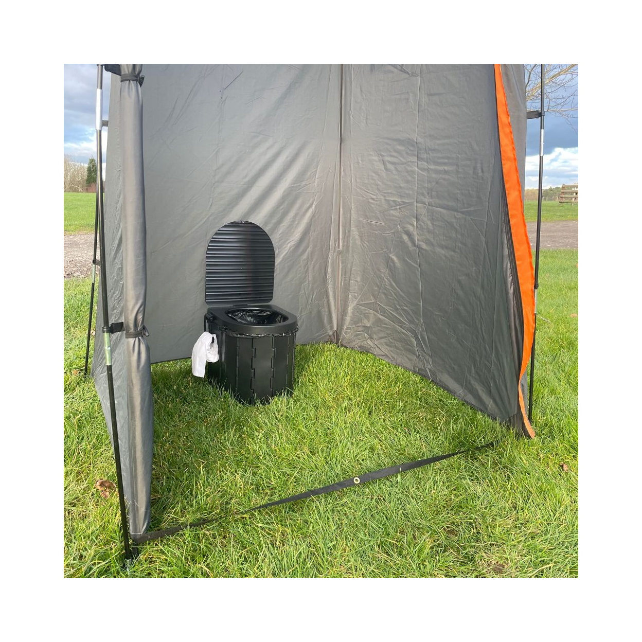 Gray and orange tent with a black composting toilet on grass