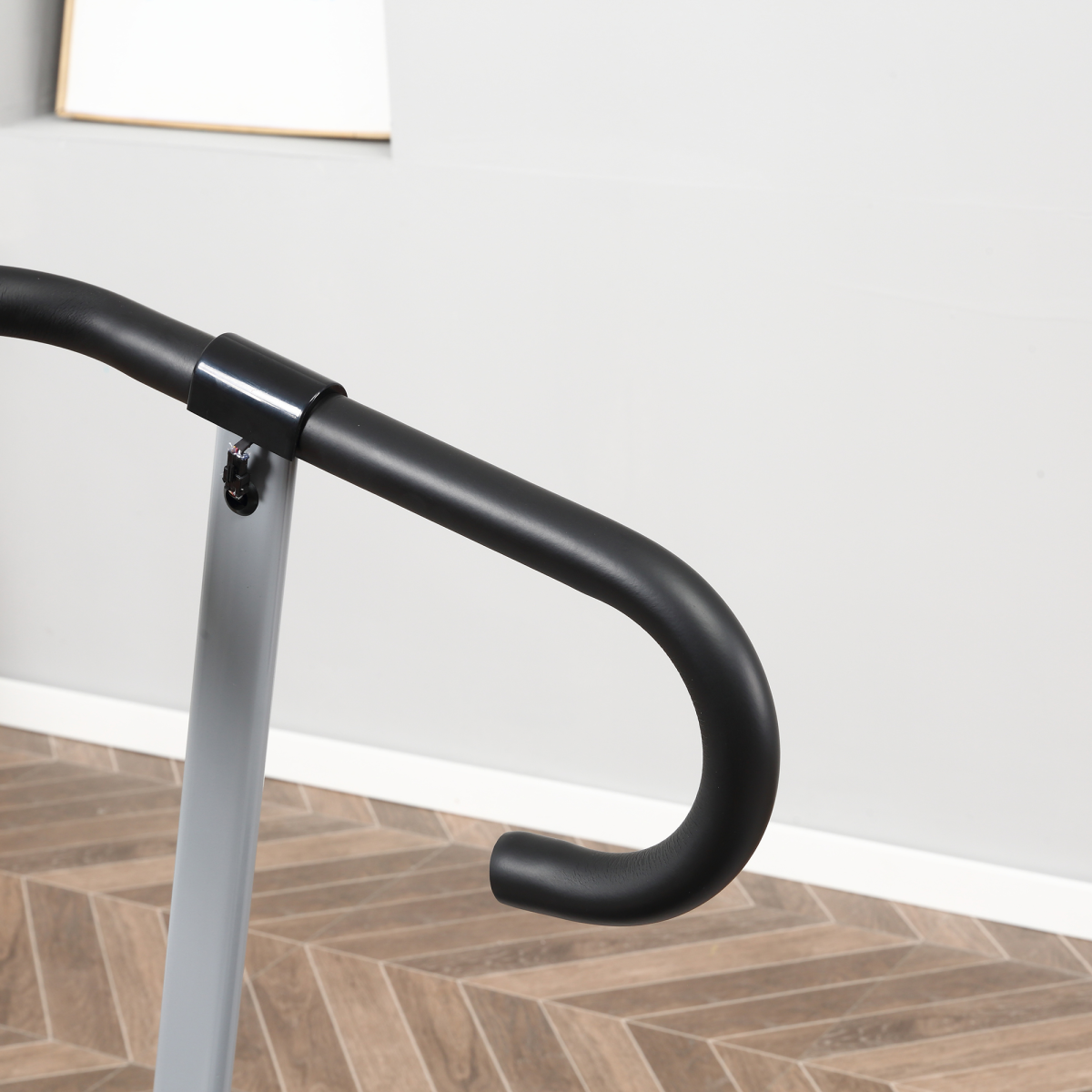 Black bicycle handlebar on a wooden floor with a white wall background