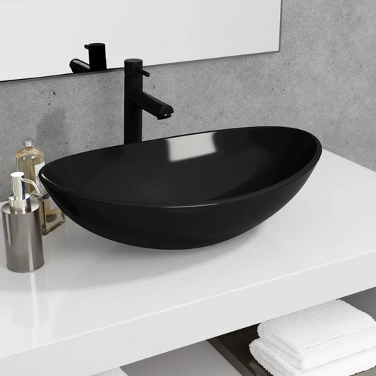 Black oval sink on a white countertop with a mirror and towels in the background.
