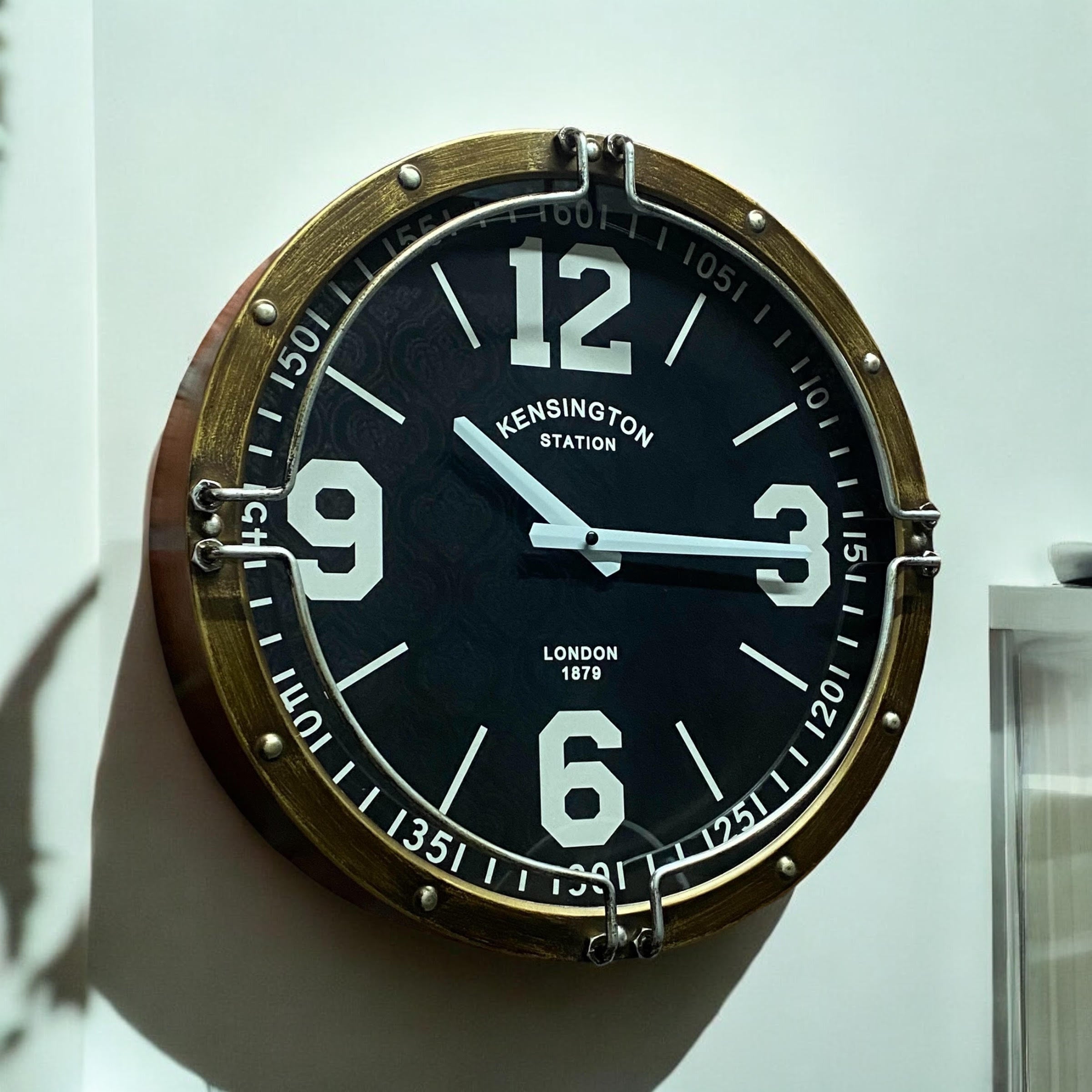 Wall clock with brass frame and black face displaying the time.