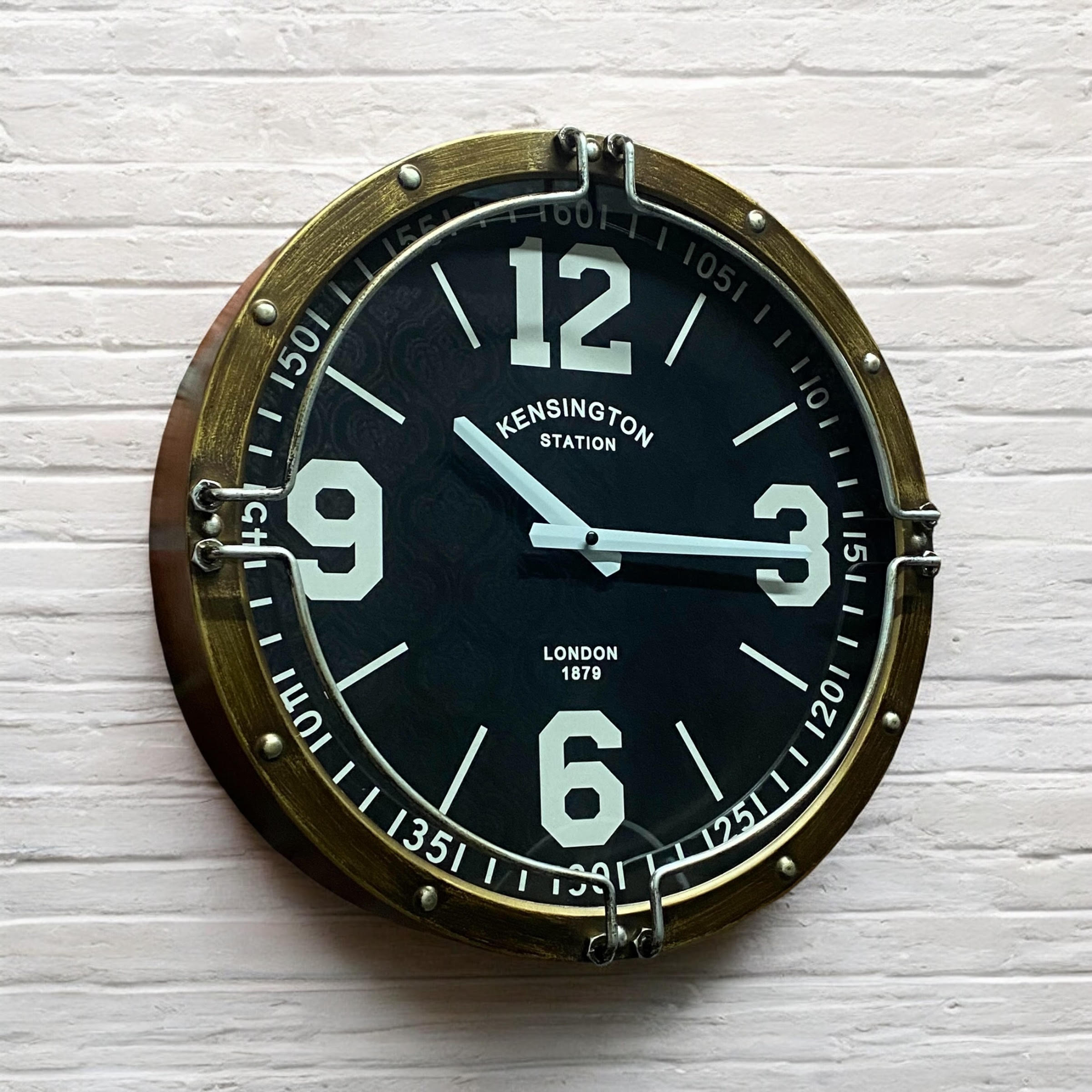 Round wall clock with brass frame and black face on a white textured background