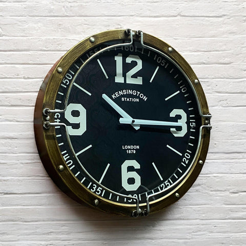 Round wall clock with brass frame and black face on a white textured background