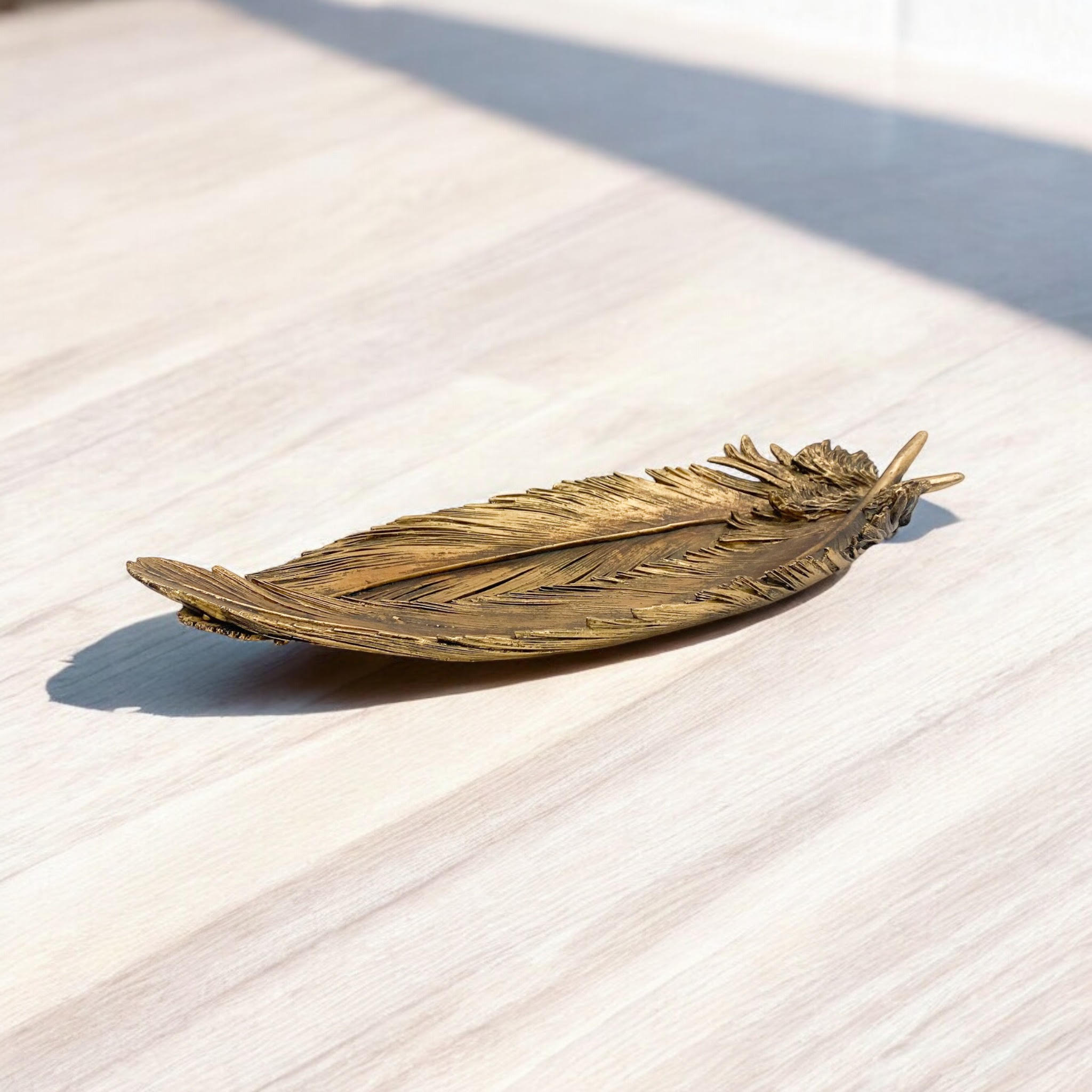 Bronze feather-shaped object on a light wooden surface
