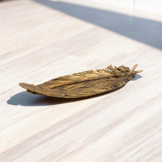 Bronze feather-shaped object on a light wooden surface